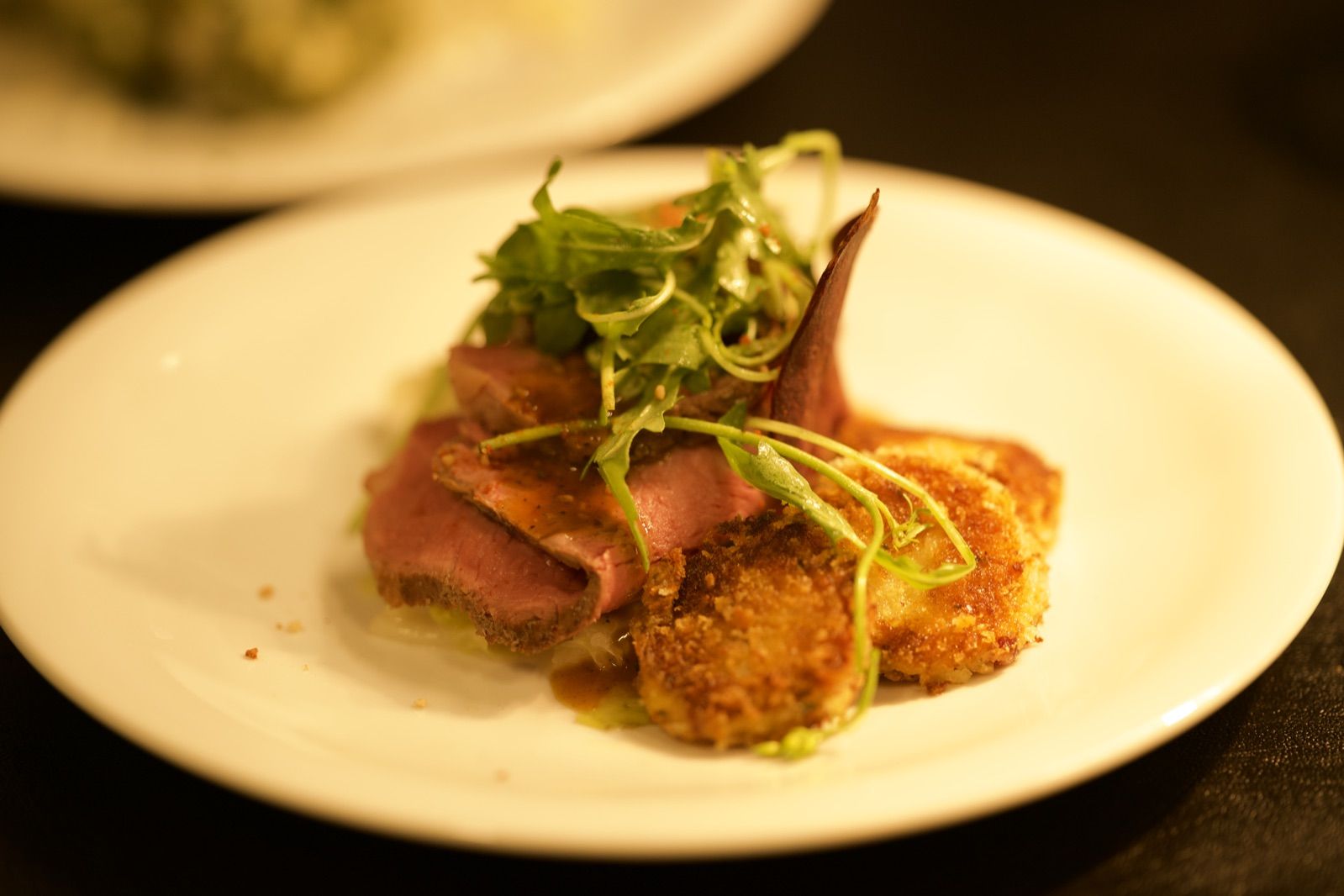 Rosa gegartes Fleisch in Scheiben auf Kartoffelrösti mit Kräutersalat auf einem weißen Teller