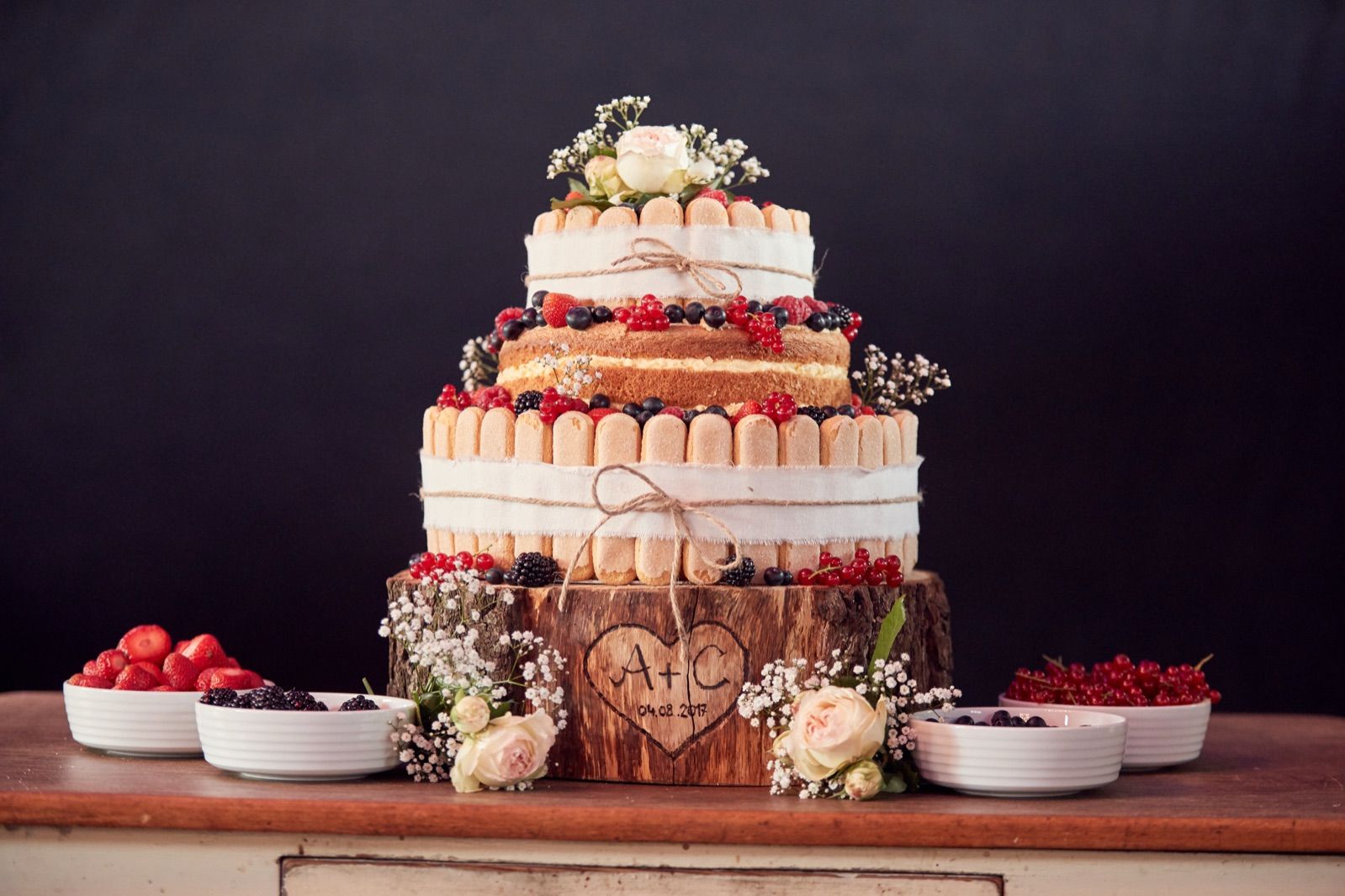 Mehrstöckige Naked-Cake-Hochzeitstorte mit Beeren und Blumen auf einer Holzscheibe
